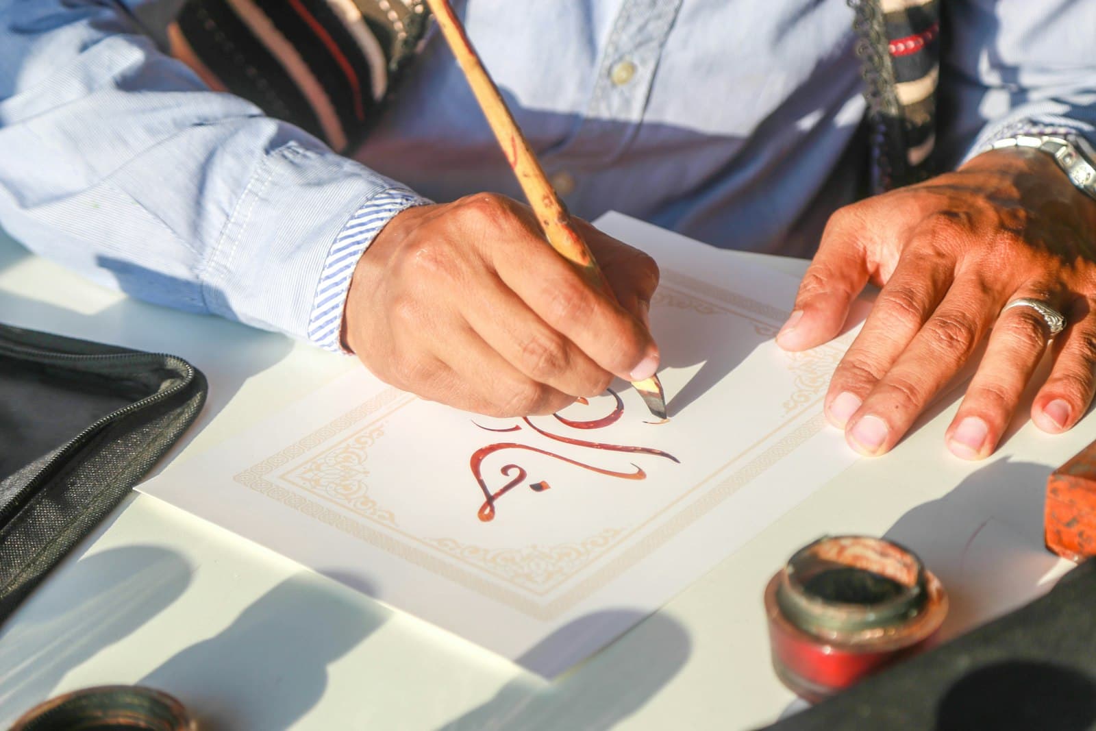 A hand writing Arabic calligraphy with a reed pen